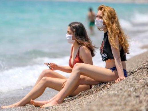 Touristinnen mit Gesichtsmaske am Strand
