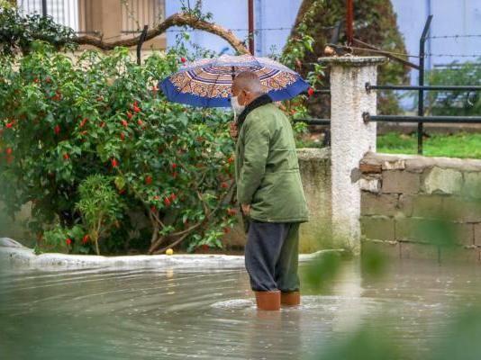 Mann steht in Gummistiefeln auf überfluteter Strasse